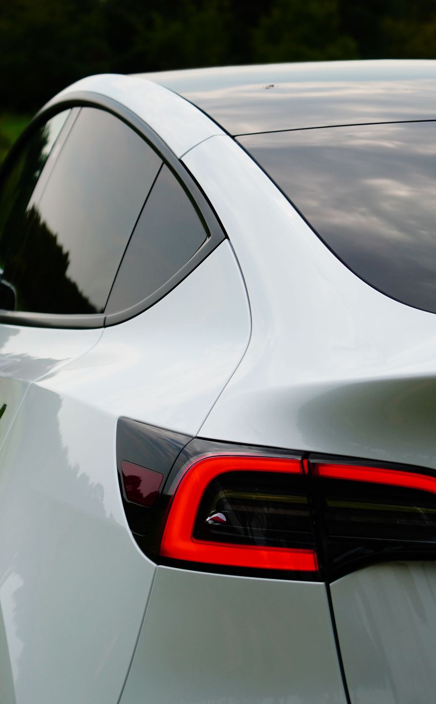 Rear quarter of a white Tesla Model Y, tail light lit